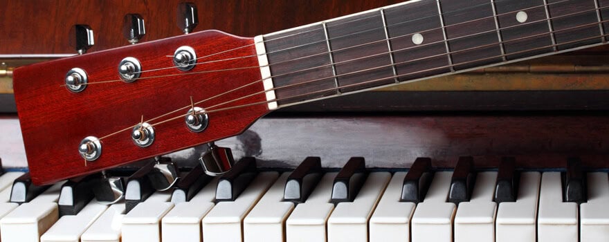 Close-up of a red guitar headstock with tuning pegs lying across white and black piano keys.